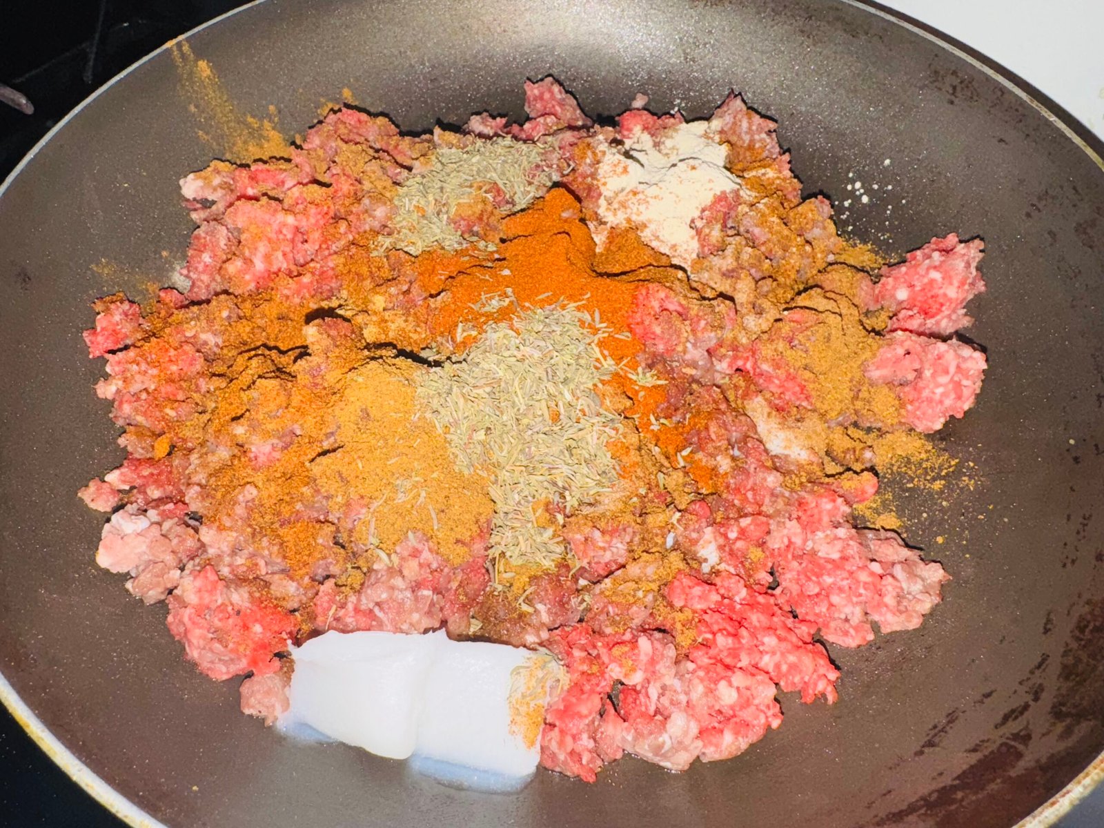 Raw ground beef in pan with spices on top